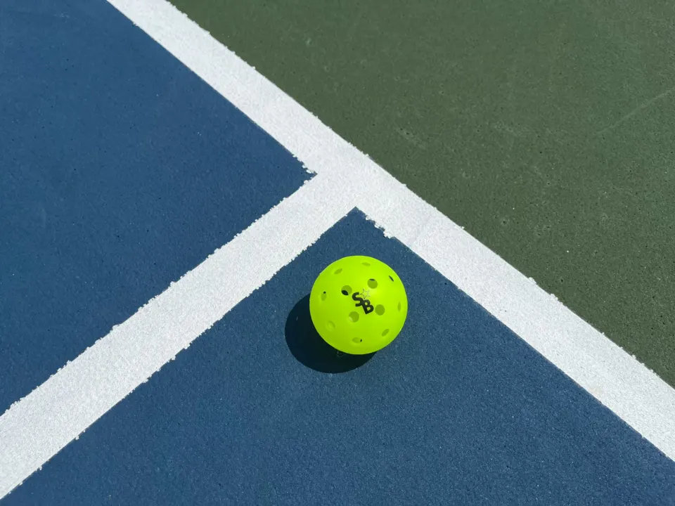 A neon pickleball resting on the court lines